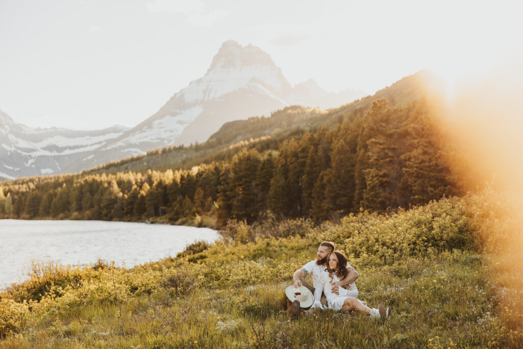 Adventure couple sitting in a field in Glacier National Park Montana beneath the mountains in the sunshine