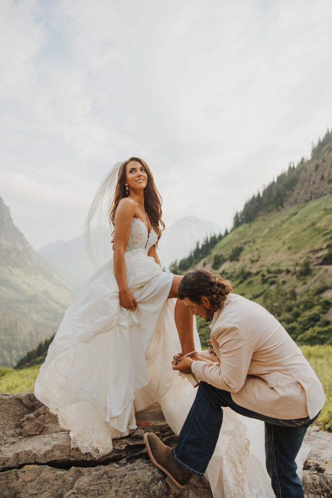 groom helping bride with her heel in glacier park